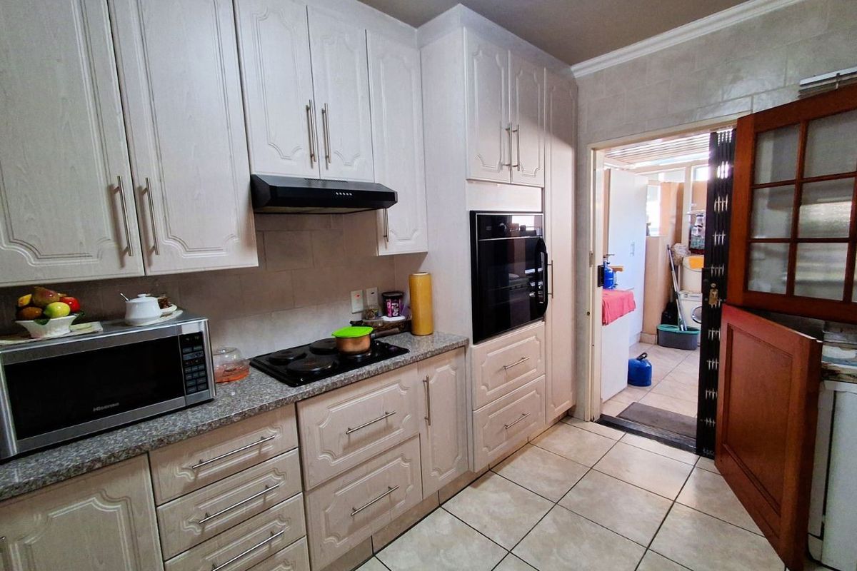 A functional kitchen featuring light-toned cabinetry, granite-look countertops, a built-in oven, and a hob with an extractor fan, leading into a separate utility area.