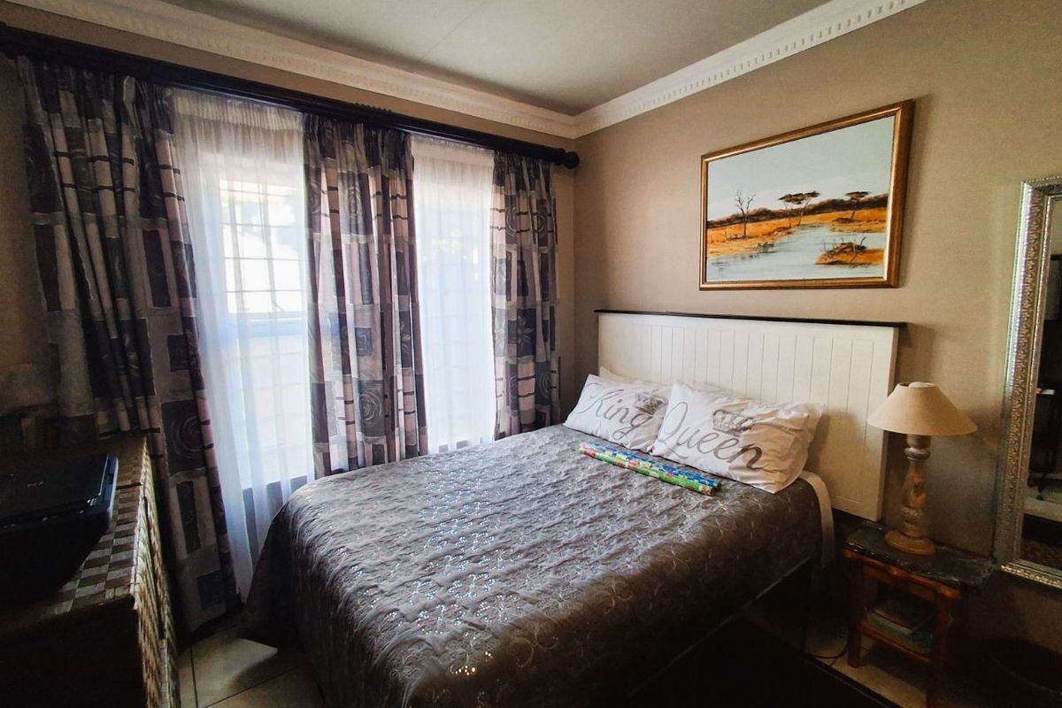 A cozy bedroom featuring tiled flooring, crown molding, and large windows with curtains, providing natural light and a comfortable living space.