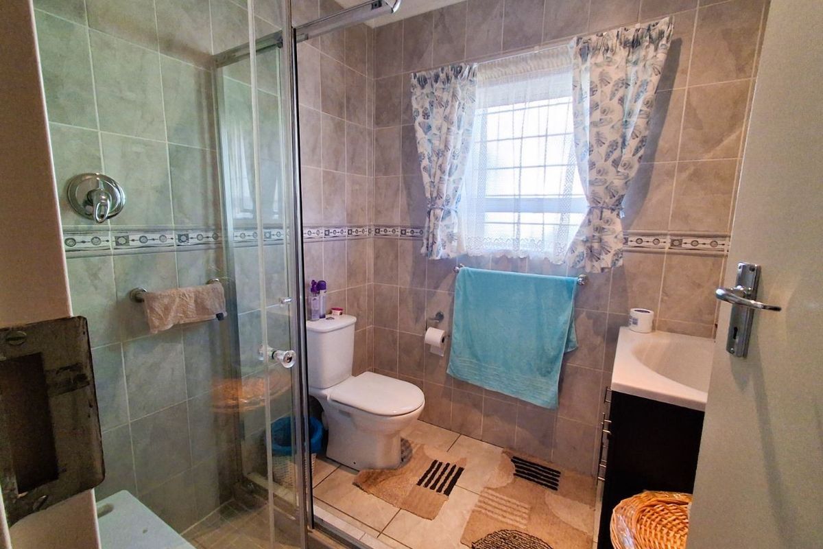 A functional bathroom featuring a glass-enclosed shower, a standard toilet, and a vanity basin with tiled walls and flooring.