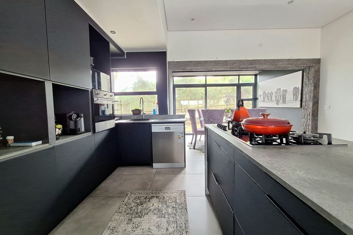 Modern kitchen featuring sleek dark cabinetry, a central island with a gas hob, integrated appliances, and large windows providing natural light and garden access.