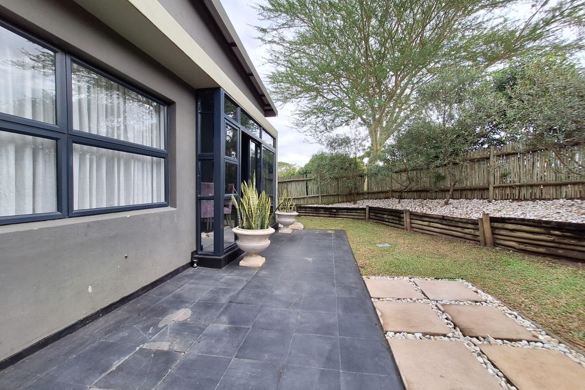 A rear exterior view featuring a tiled patio, landscaped garden with retaining walls, and a timber fence boundary.