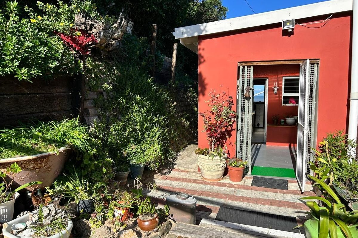 A rear exterior view featuring a red-painted building facade, security gate entrance, and a landscaped garden area with brick paving and retaining walls.