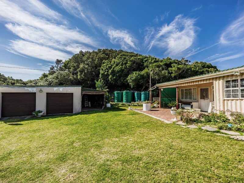 Rear exterior view featuring a lawn, paved patio area, double garage, and multiple water storage tanks set against a natural backdrop.