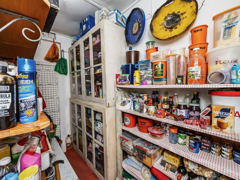 A functional scullery or pantry area featuring built-in cabinetry and extensive fixed shelving for storage.