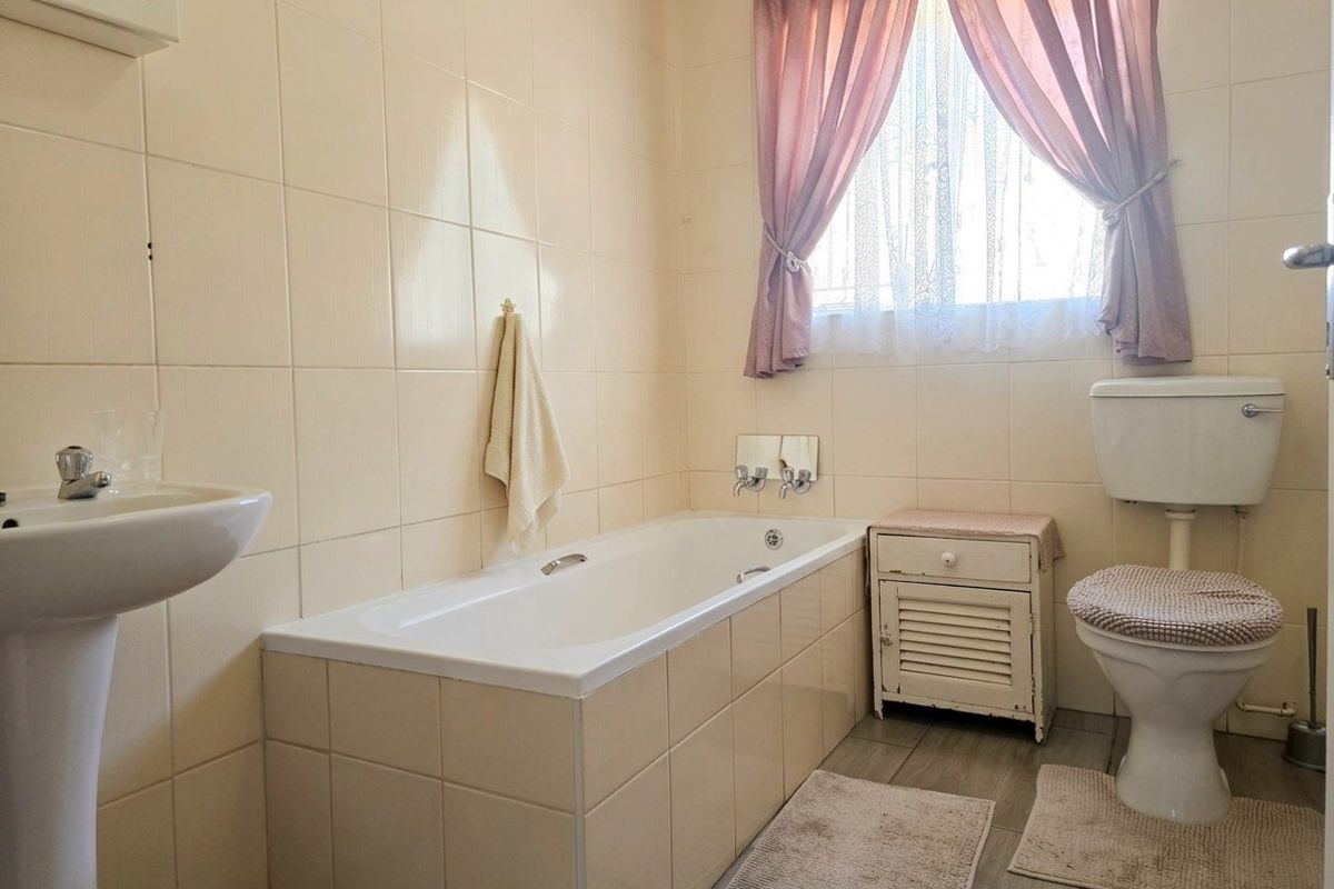 A functional bathroom featuring a built-in bathtub, pedestal basin, and standard toilet, finished with neutral wall tiles and wood-look flooring.