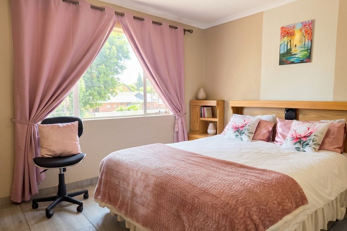 A well-lit bedroom featuring tiled flooring, a built-in wooden headboard with integrated shelving, and a large window with curtain fixtures.