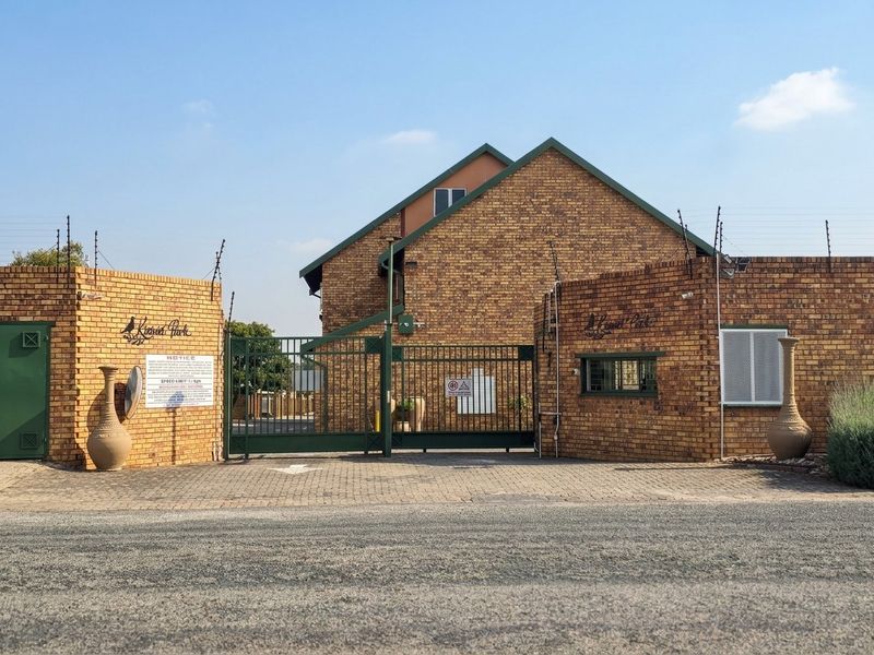 Front entrance view of the townhouse complex featuring a brick perimeter wall, secure metal gate, and electric fencing.