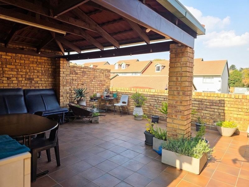 A covered patio area featuring exposed brick walls, tiled flooring, and a timber-framed roof structure, offering an open-air space for outdoor relaxation.