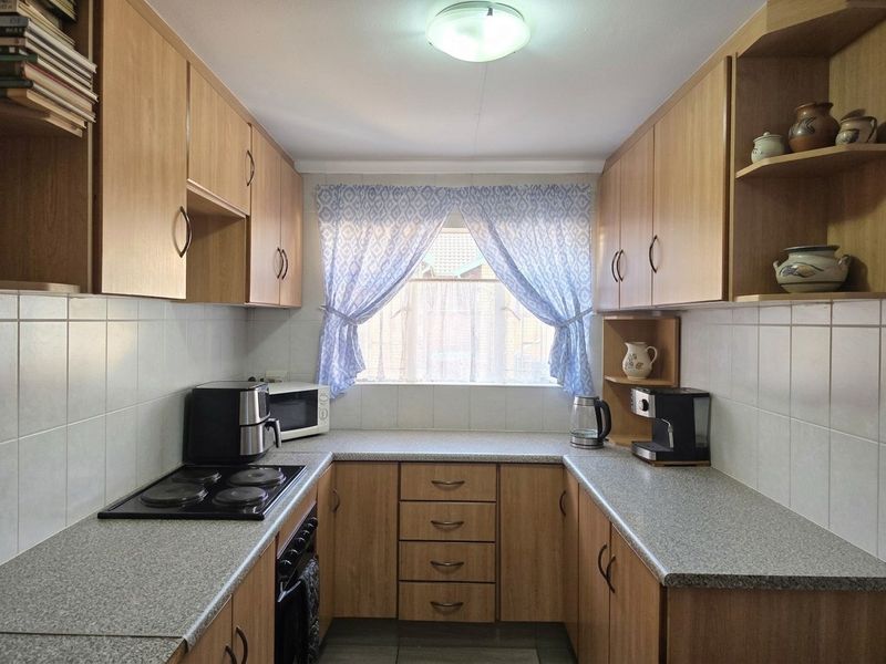 A functional galley-style kitchen featuring light wood-finish cabinetry, laminate countertops, tiled splashbacks, and a built-in electric hob and oven.