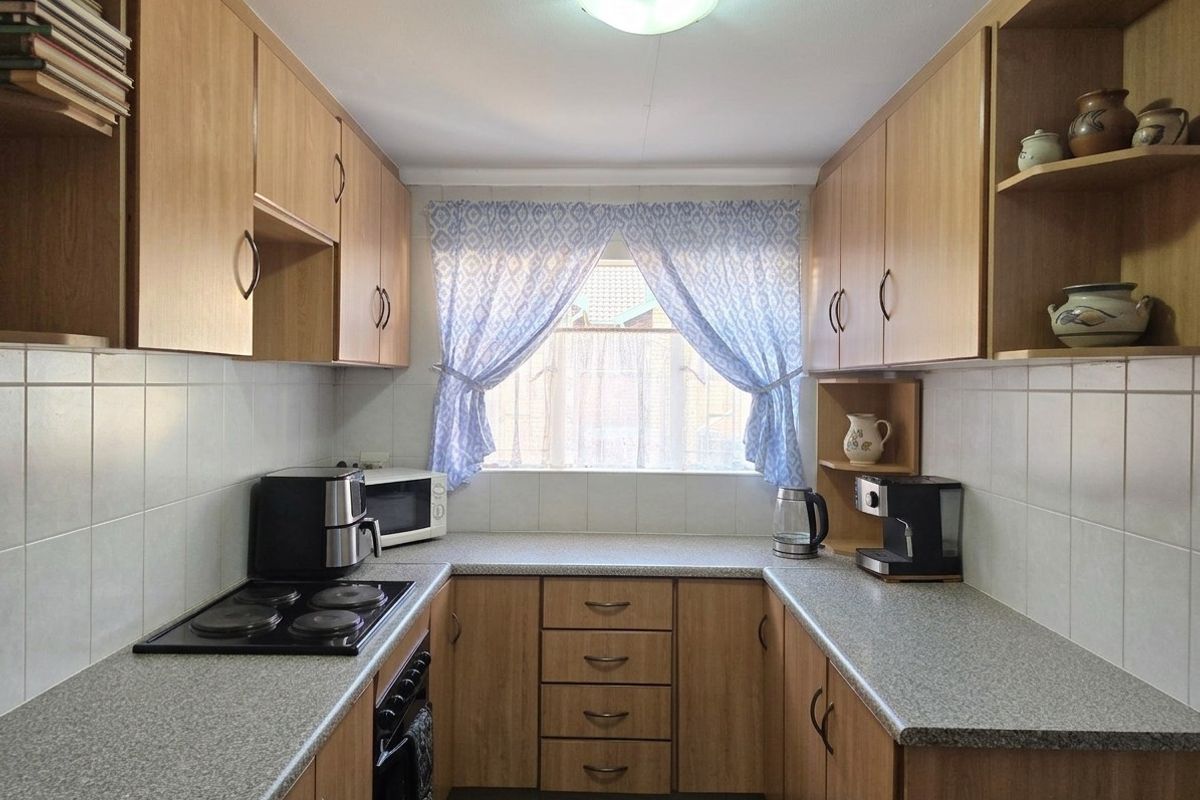 A functional galley-style kitchen featuring light wood-finish cabinetry, laminate countertops, tiled splashbacks, and a built-in electric hob and oven.