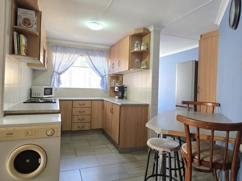 A functional kitchen featuring light wood cabinetry, tiled splashbacks, a built-in hob, and an integrated breakfast nook area.