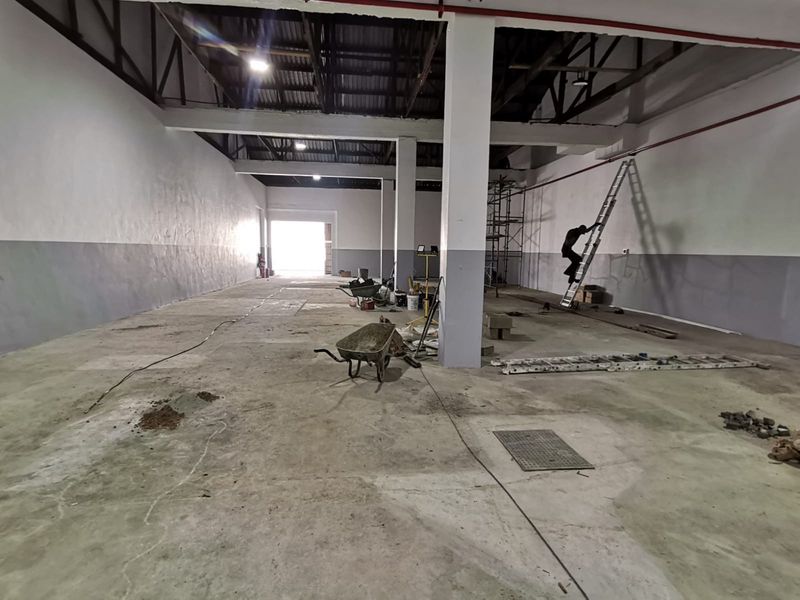 Spacious industrial warehouse interior featuring high ceilings, exposed steel trusses, concrete flooring, and fire suppression systems, currently undergoing maintenance and renovation.