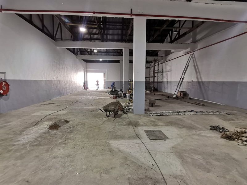 Spacious industrial warehouse unit featuring high ceilings, exposed structural beams, concrete flooring, and fire suppression piping, currently undergoing maintenance and renovation.