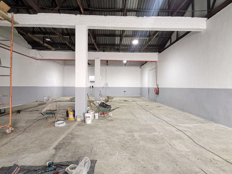 Spacious industrial warehouse unit featuring high ceilings, exposed structural beams, concrete flooring, and fire safety equipment, currently undergoing maintenance.