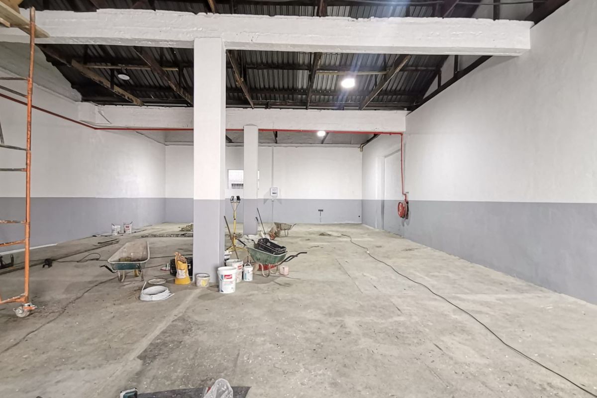 Spacious industrial warehouse unit featuring high ceilings, exposed structural beams, concrete flooring, and fire safety equipment, currently undergoing maintenance.