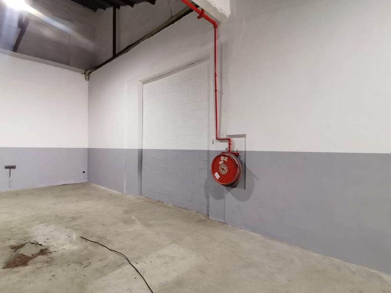 Industrial warehouse space featuring painted block walls, concrete flooring, and a wall-mounted fire hose reel.