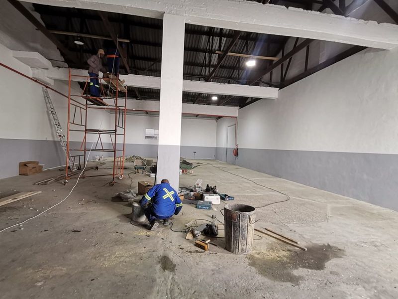 Spacious industrial warehouse interior currently undergoing maintenance and renovation, featuring high exposed ceilings, concrete flooring, and open-plan layout.