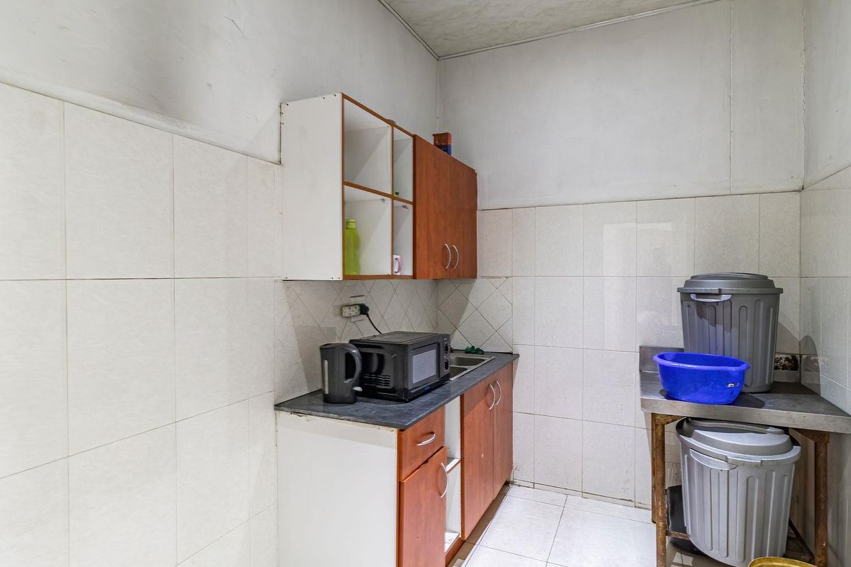 A compact industrial kitchenette featuring tiled walls, basic cabinetry, and a stainless steel prep surface.