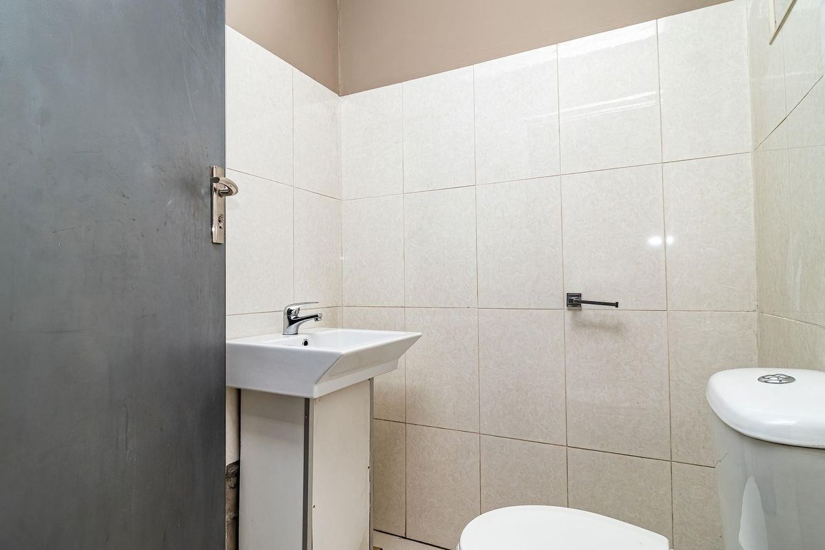 A functional bathroom featuring a wall-mounted basin with vanity cabinet, a standard toilet, and full-height wall tiling.