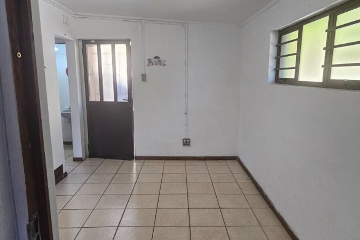 An empty, functional room featuring neutral ceramic floor tiles, a window with security bars, and a door leading to an adjacent space.