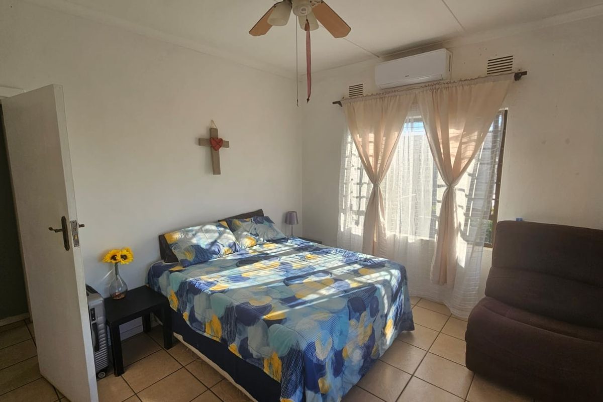 A functional bedroom featuring tiled flooring, a wall-mounted air conditioning unit, and a ceiling fan, providing a comfortable and practical living space.