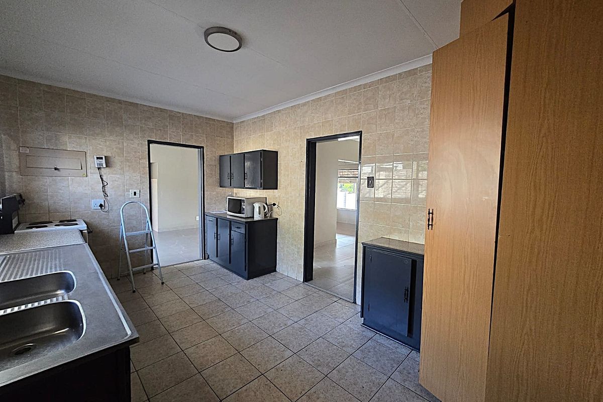 Functional kitchen featuring tiled flooring, ample built-in cabinetry, a double bowl stainless steel sink, and a tiled splashback.