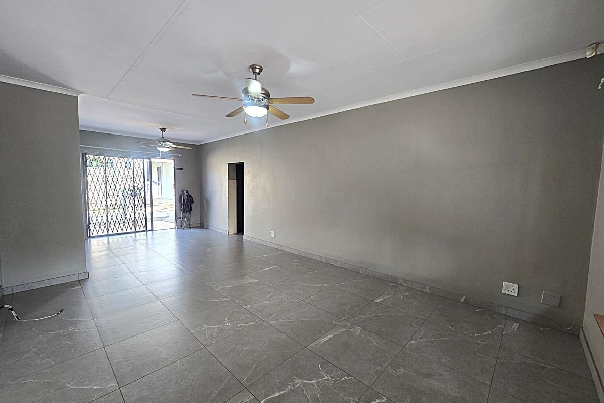 Spacious, empty living area featuring large format grey floor tiles, dual ceiling fans, and a secure metal gate leading to the exterior.