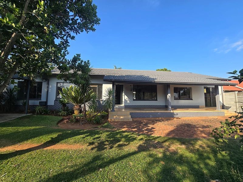 Front elevation of a well-maintained single-story house featuring a tiled roof, covered patio, and a paved driveway set within a landscaped garden.