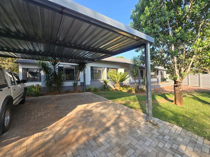 Front exterior view of the house featuring a metal carport, paved driveway, and well-maintained garden area.