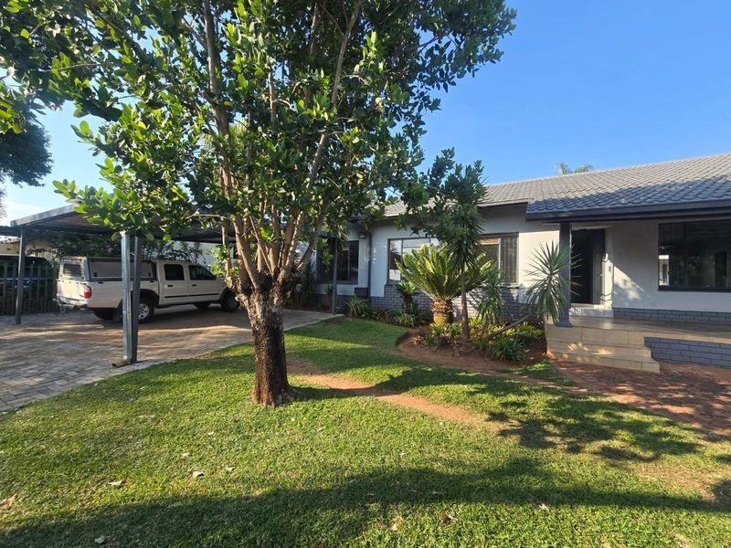 Front view of the property featuring a paved driveway, carport, landscaped garden, and a well-maintained brick and tile facade.