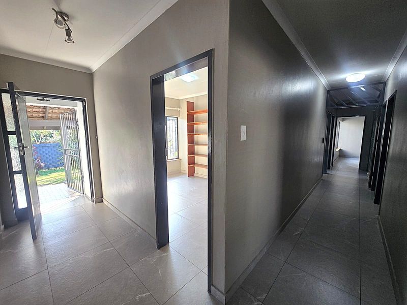 A spacious hallway featuring neutral tiled flooring, leading to an adjacent room with built-in shelving and access to the exterior via a security gate.