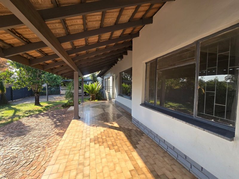 A covered outdoor patio featuring tiled flooring and exposed timber beams, providing a sheltered transition space between the home and the garden.