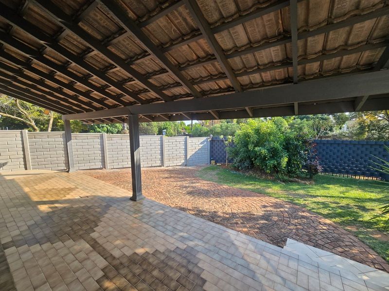 A spacious covered patio area featuring tiled flooring, overlooking a private garden with paved pathways and secure boundary walls.