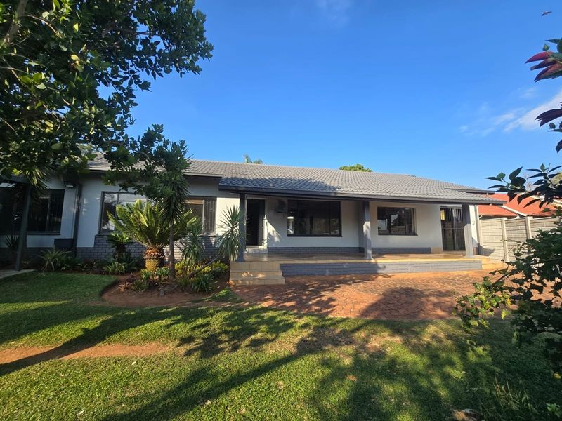 Rear view of the house featuring a covered patio, brick paving, and a well-maintained garden area.