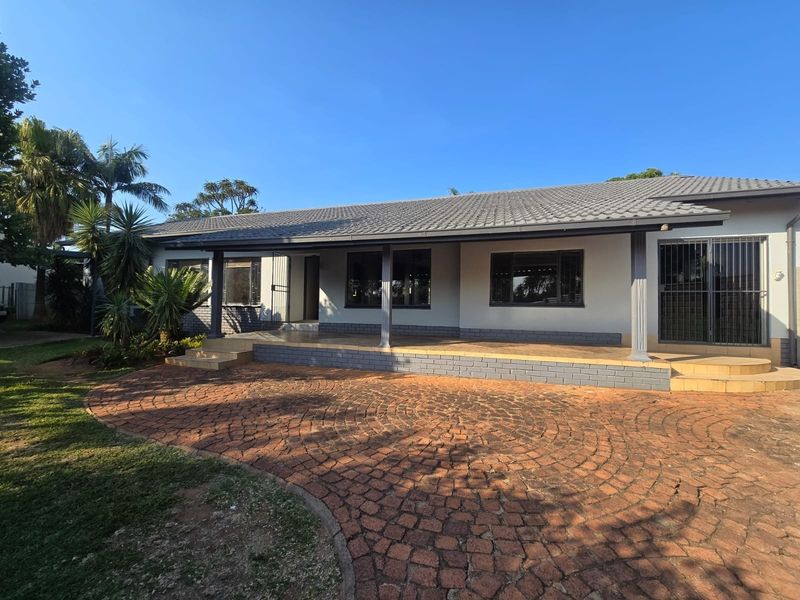 Front elevation of a single-story house featuring a covered patio, tiled roof, and a circular brick-paved driveway.