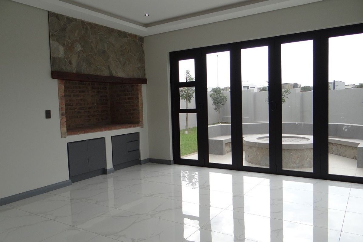 Spacious living area featuring a built-in braai with stone detailing, polished marble-look floor tiles, and large stacking doors opening to an outdoor patio.