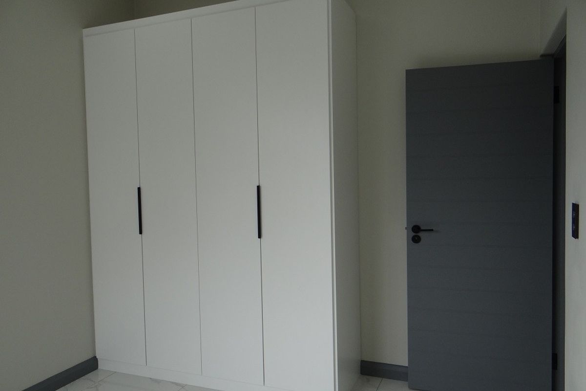 A clean, modern bedroom featuring white built-in wardrobes, grey internal door, and light-colored tiled flooring.