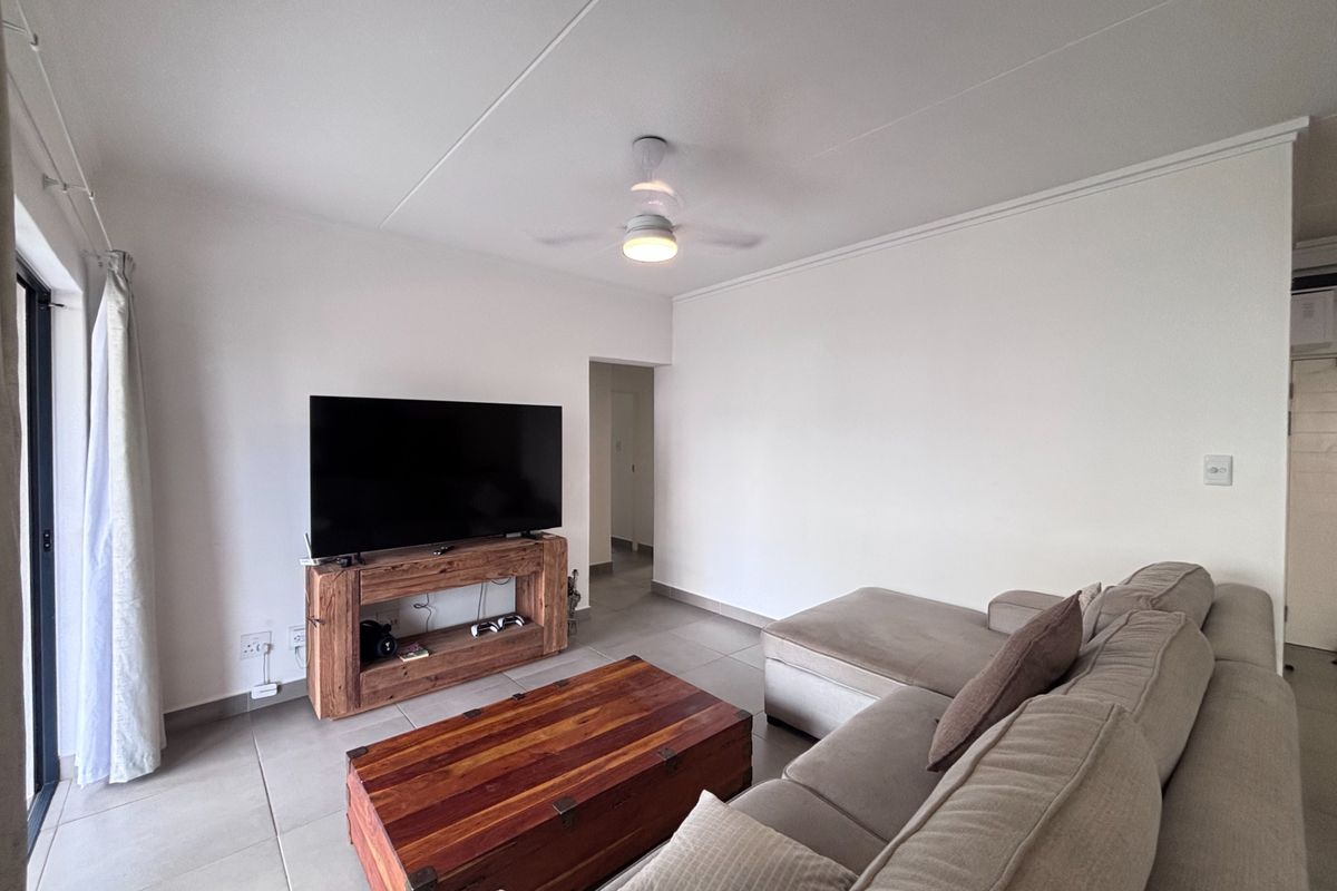 A bright living room featuring neutral floor tiles, a ceiling fan, and sliding glass doors providing access to the outdoor area.