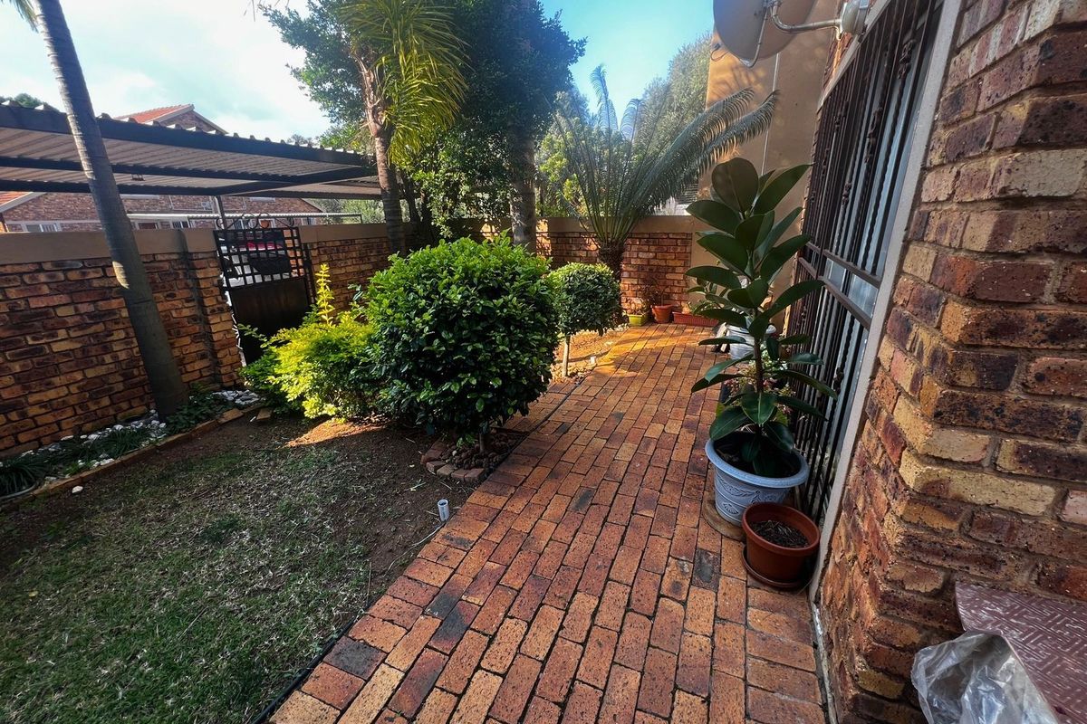 A private rear garden area featuring a brick-paved pathway, perimeter brick walling, and established landscaping.