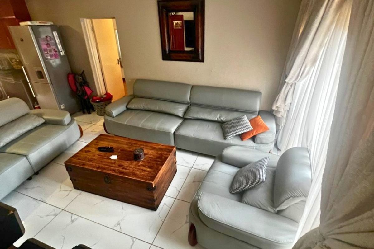 A living room area featuring large format floor tiles and access to an adjacent kitchen space.