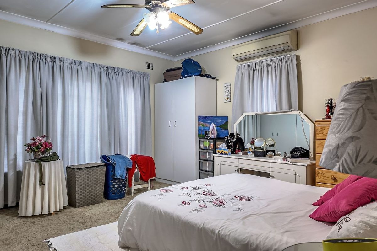 A spacious bedroom featuring carpeted flooring, a ceiling fan, and a wall-mounted split-system air conditioner, with visible water staining on the ceiling.