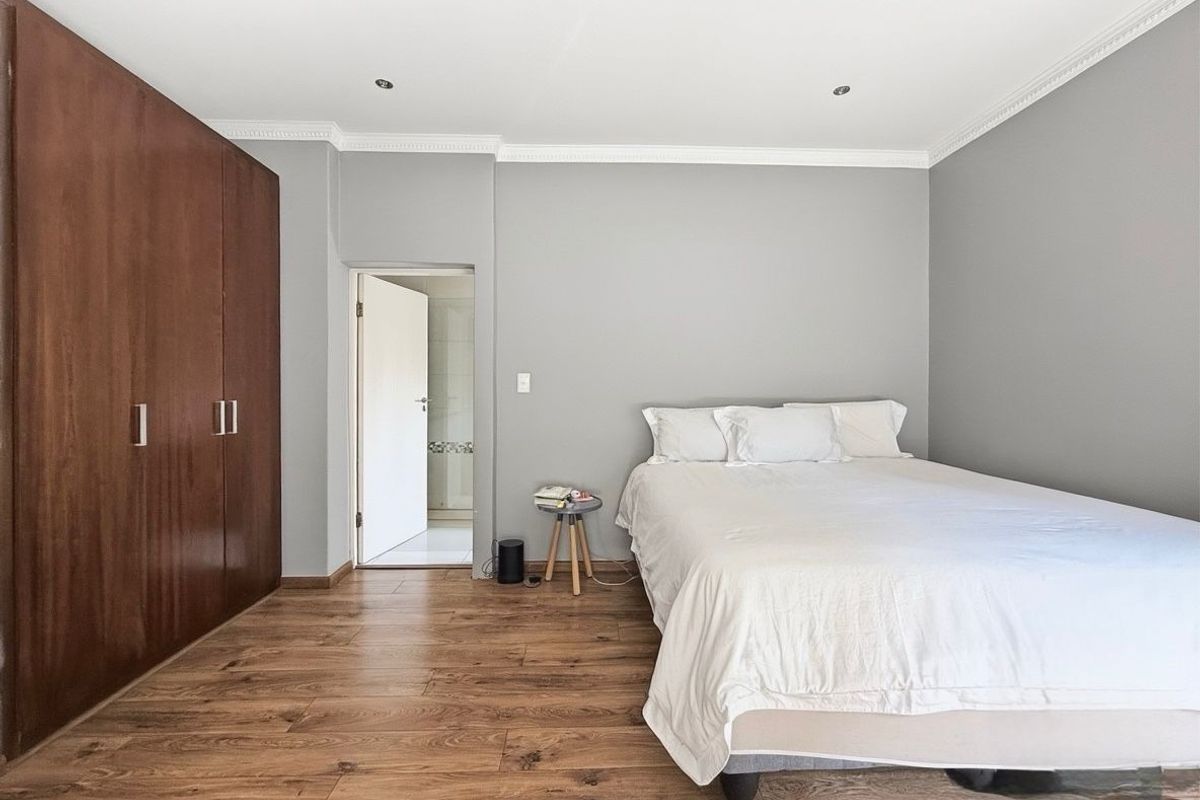 A well-maintained bedroom featuring wood-look flooring, built-in wooden cabinetry, and an en-suite bathroom entrance.