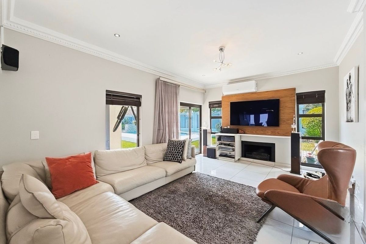 Spacious living room featuring tiled flooring, a built-in fireplace with wood-panel feature wall, and large sliding doors providing access to the outdoor pool area.