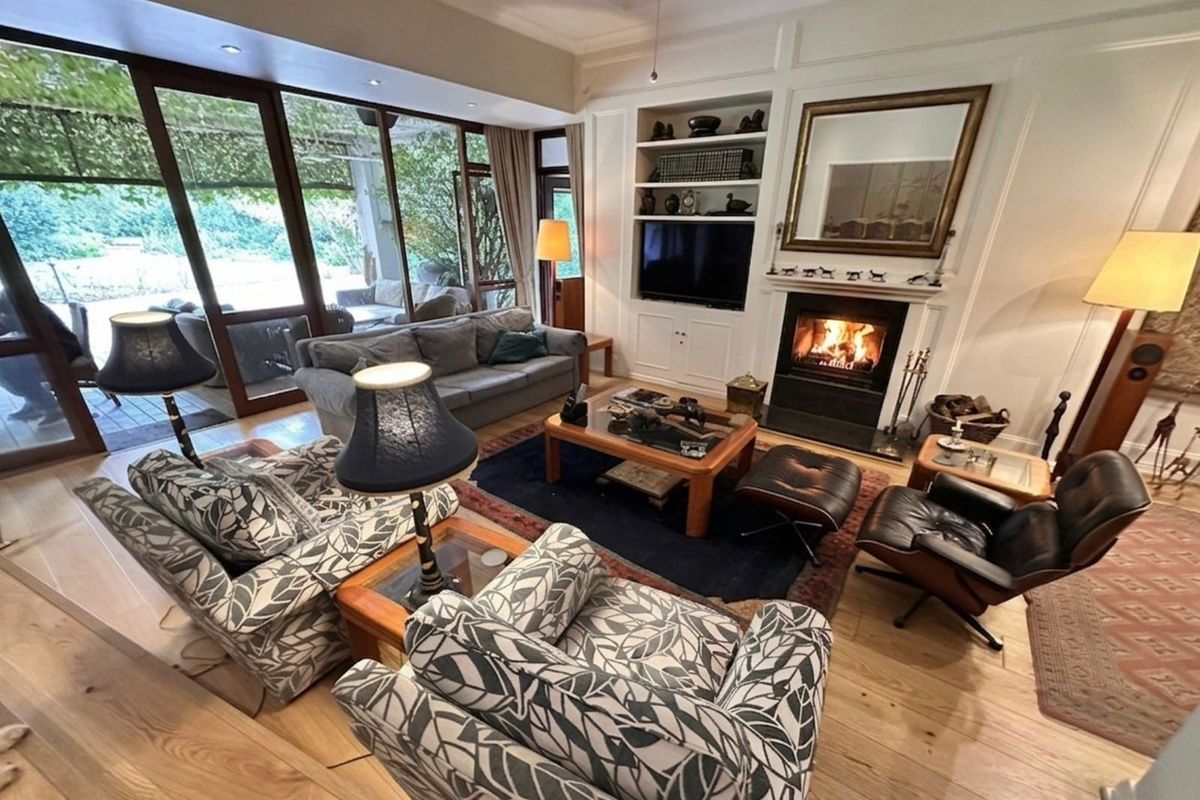 Spacious living room featuring light timber flooring, a built-in fireplace with mantle, custom cabinetry, and large sliding glass doors opening to a covered patio.