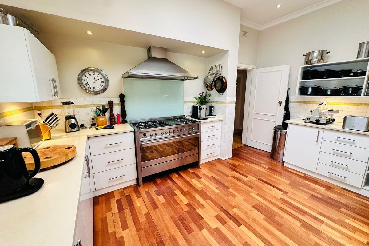 A well-maintained kitchen featuring white cabinetry, a stainless steel gas range with extractor hood, tiled splashbacks, and warm timber flooring.