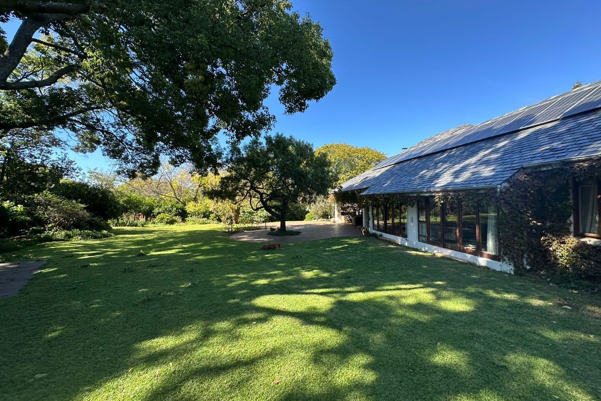 A spacious rear garden featuring a well-maintained lawn, mature trees, and a paved patio area adjacent to the house with integrated solar panels.