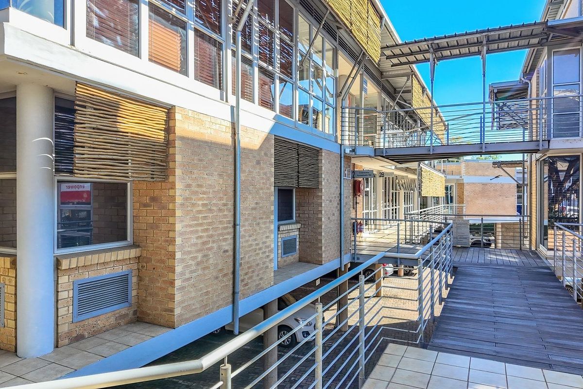Modern commercial office complex featuring face-brick facade, elevated walkways, steel railings, and large glass windows providing ample natural light.