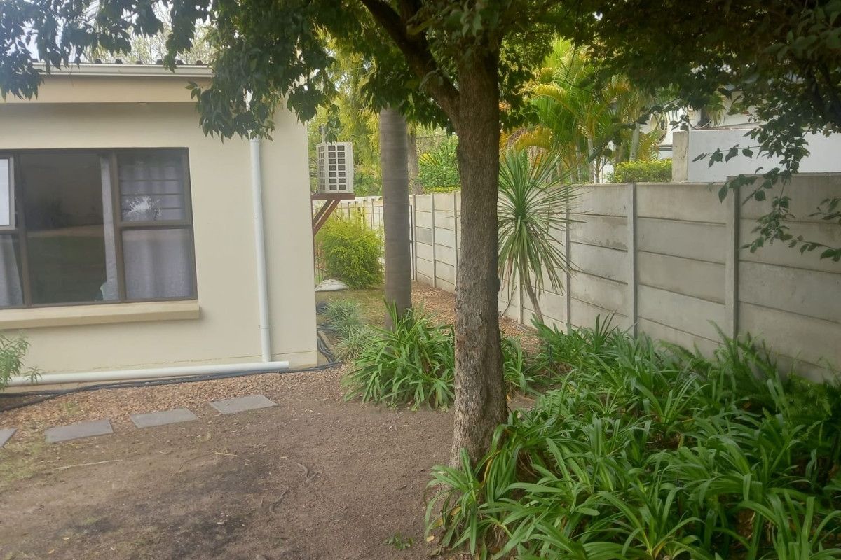 A view of the rear garden area featuring a concrete boundary wall, established trees, and a side elevation of the house.