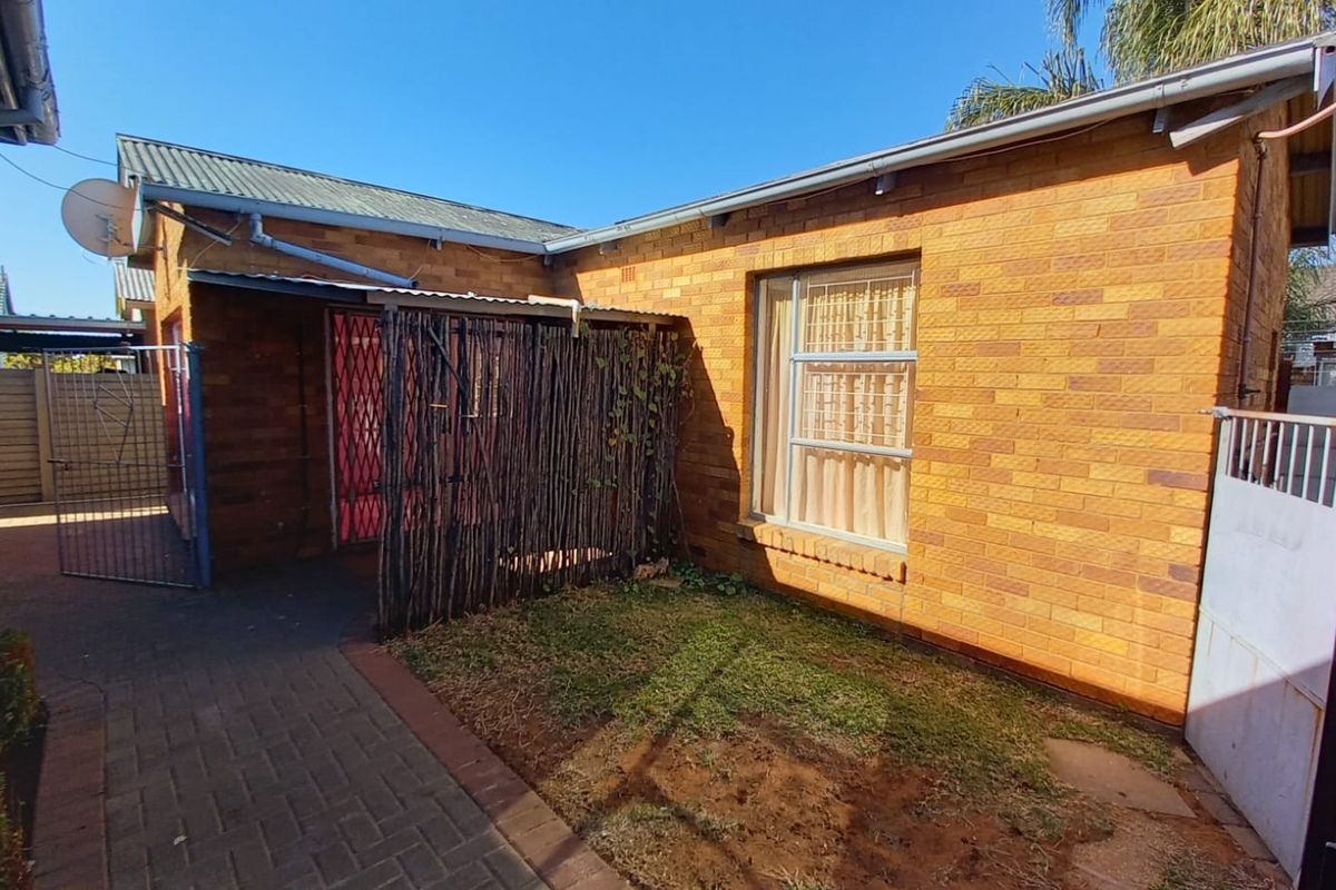 A view of the rear exterior of the house featuring face brick walls, a paved walkway, and a small garden area.