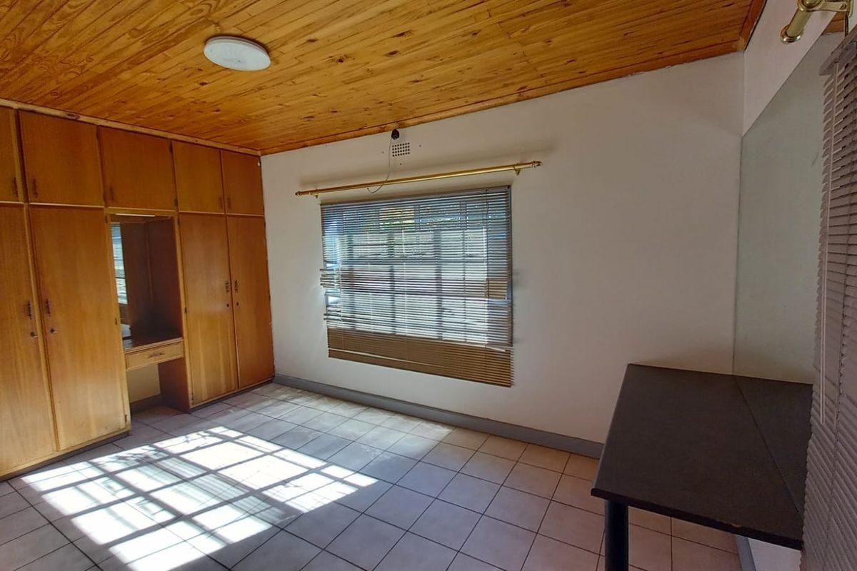 A bedroom featuring built-in wooden cabinetry, tiled flooring, and a timber-clad ceiling with a window fitted with horizontal blinds.